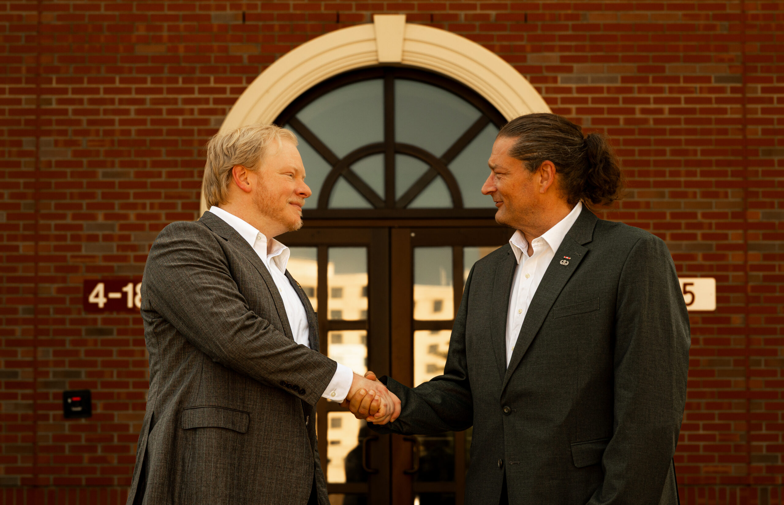 Cadman Kiker and Will M. Helixon shaking hands outdoors in front of a brick building