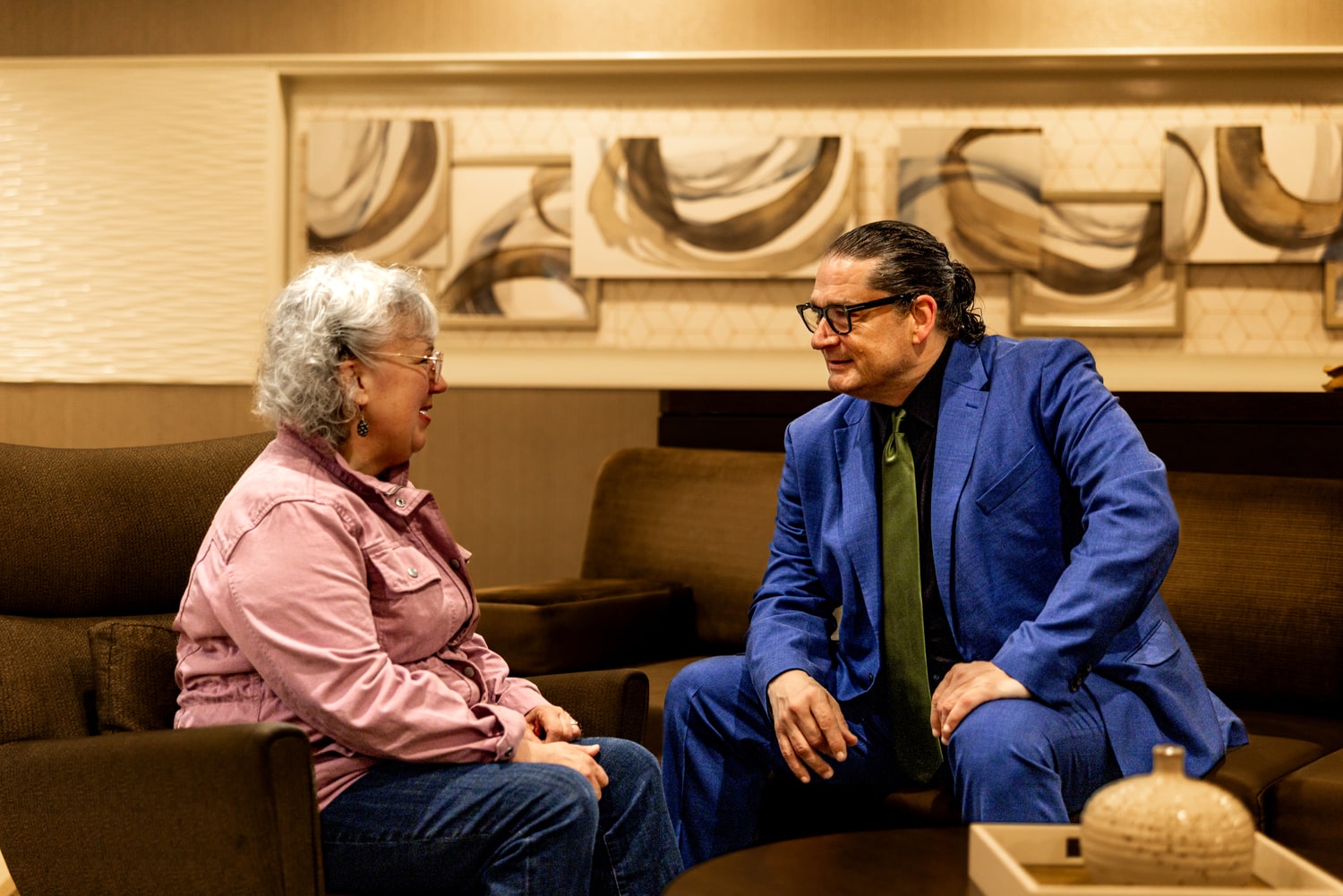 Genie Hughes and Will M. Helixon sitting and conversing in a lounge