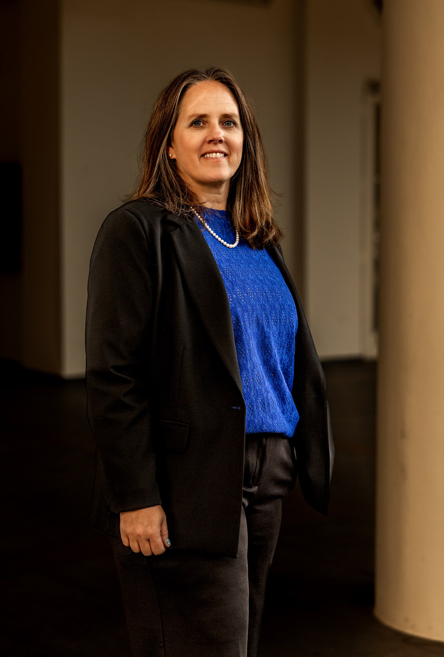 Kyle Meisner in a black blazer and necklace, standing near an interior column