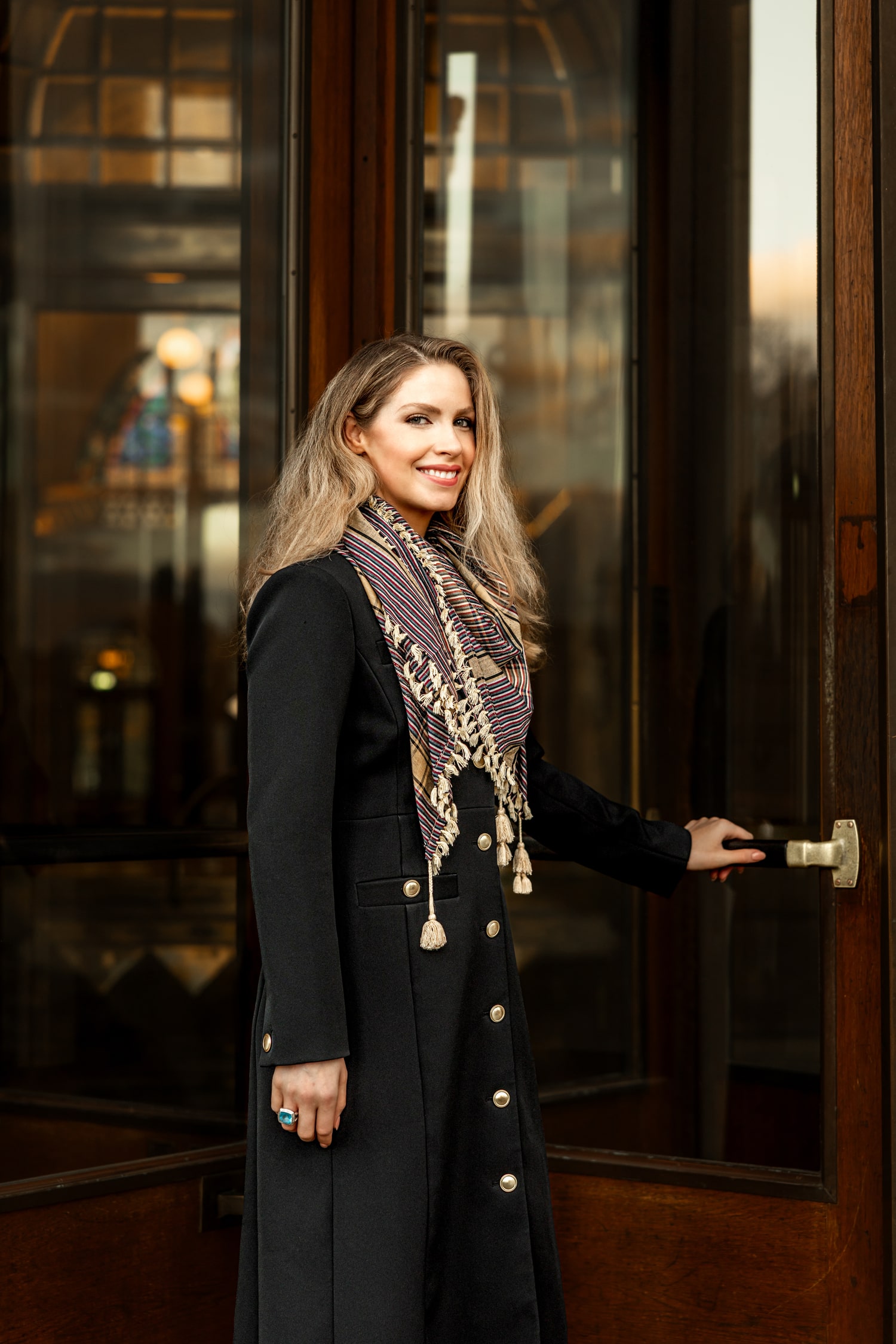 Laura Kiker wearing a dark coat and patterned scarf, opening a wooden door