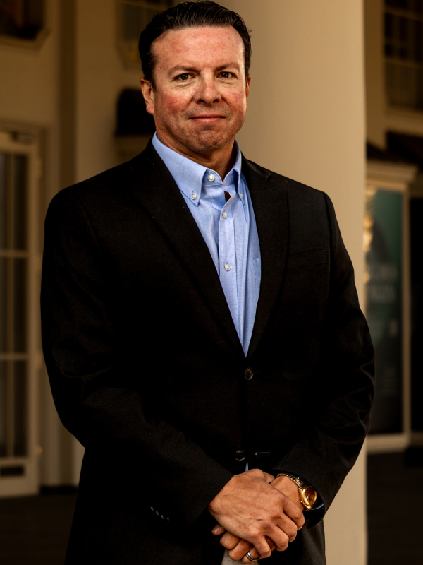 Military attorney Andre Le Blanc standing with hands clasped, wearing black suit and light blue shirt indoors