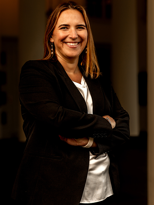 Elizabeth Talarico in a black suit and white blouse, standing with arms crossed in a hallway