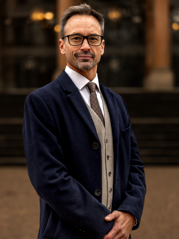 Military attorney John Caulwell standing with hands clasped, wearing navy blazer and patterned tie