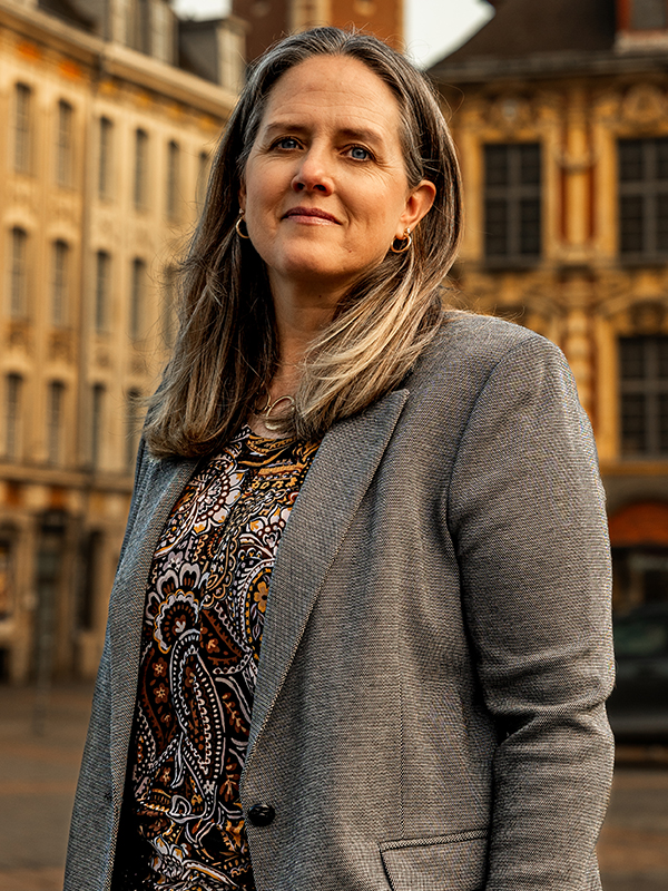 Military attorney Kyle Meisner standing outdoors, wearing patterned blouse and grey blazer with buildings in the background