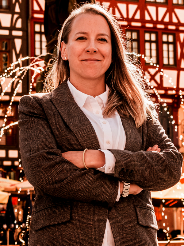 Military attorney Natalia Helmsing standing outdoors, wearing brown plaid blazer and white shirt with arms crossed