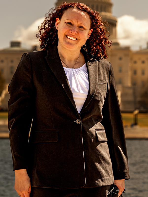 Military attorney Victoria Camire standing outdoors in front of a government building, wearing black suit and white blouse