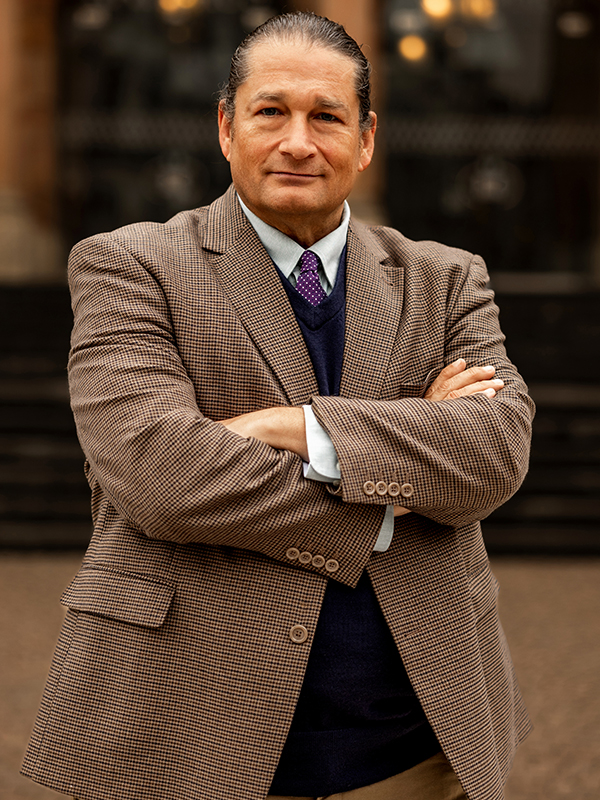 Military attorney Will M. Helixon standing with arms crossed in brown checkered suit jacket