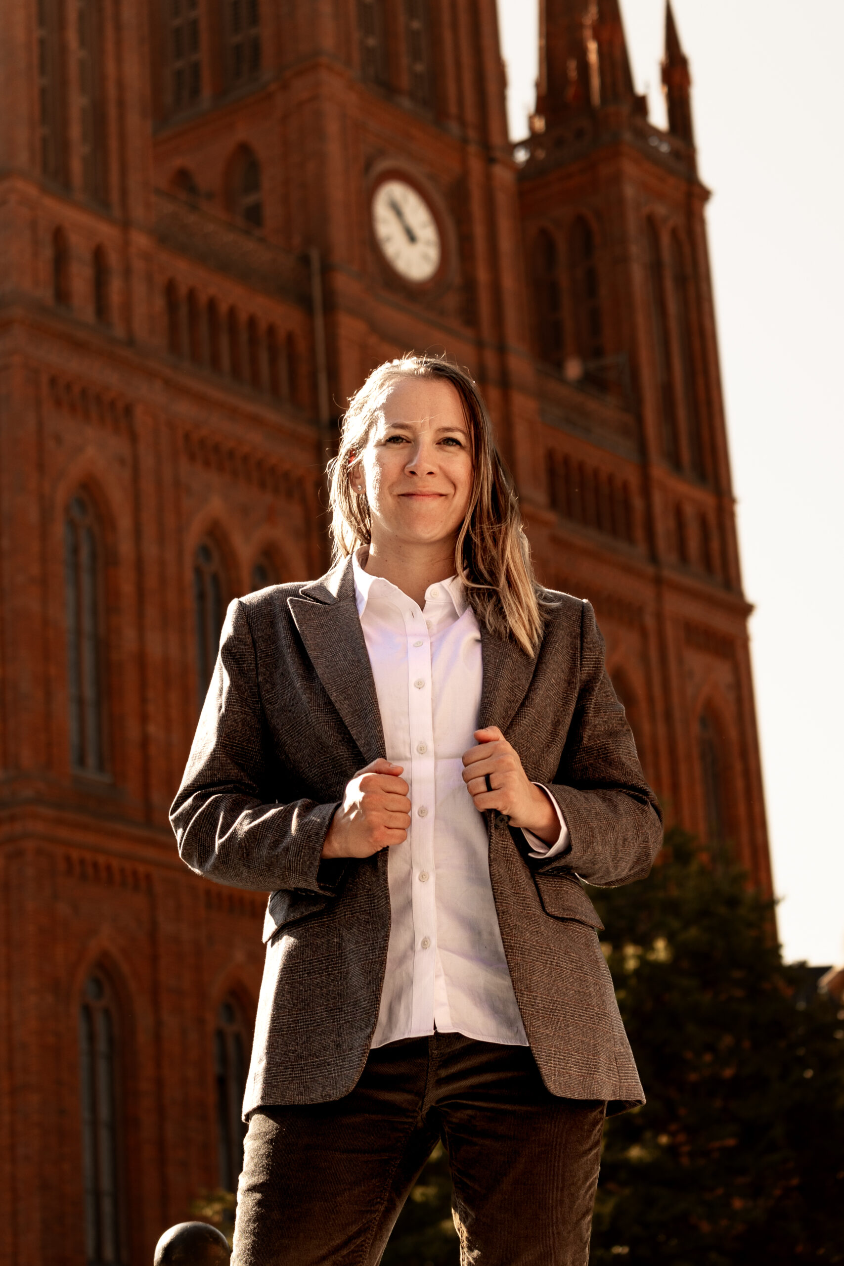 Natalia Helmsing outdoors in a brown blazer, smiling with historic brick clock tower in background