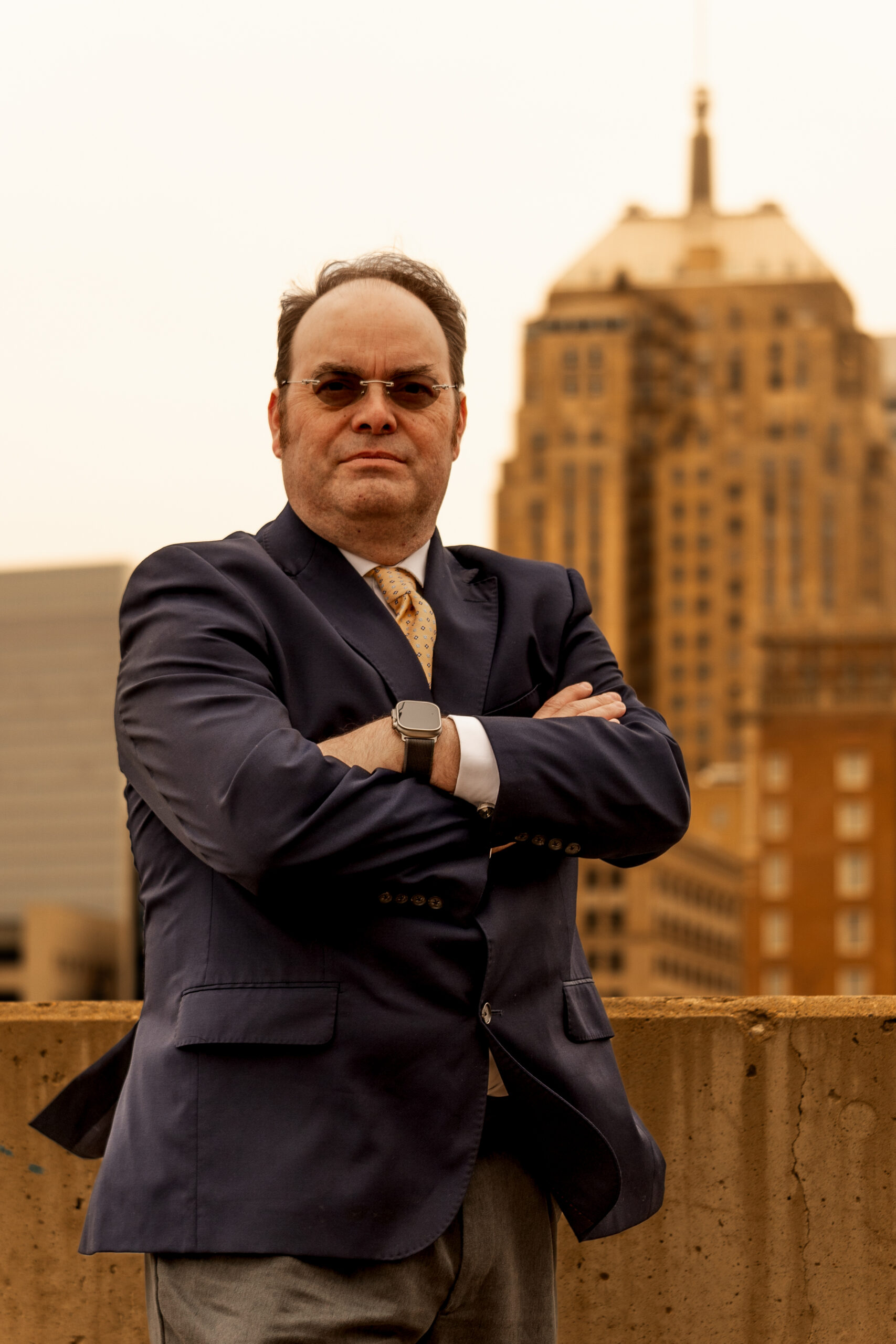 Robert Newark standing with arms crossed on a rooftop with tall buildings behind