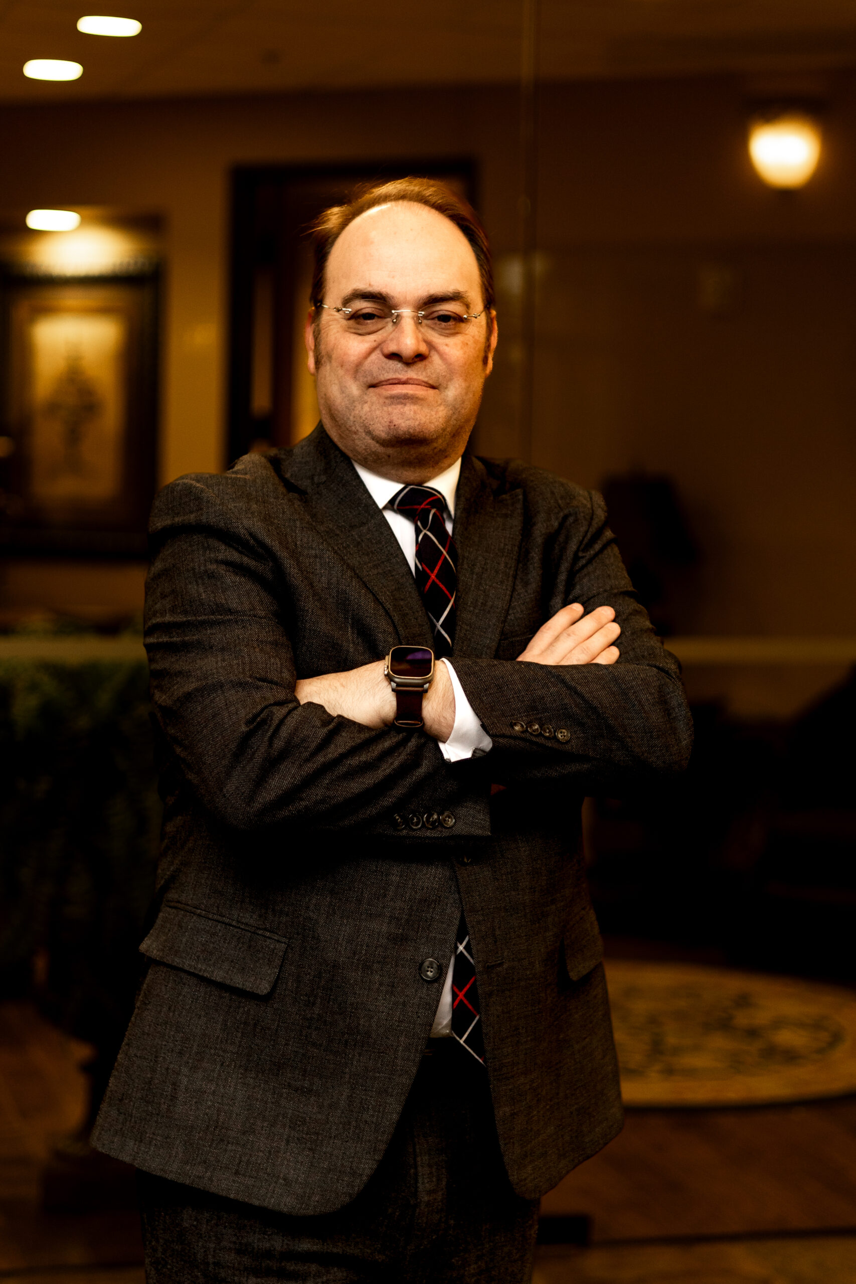 Robert Newark standing with arms crossed in a suit inside a warmly lit office