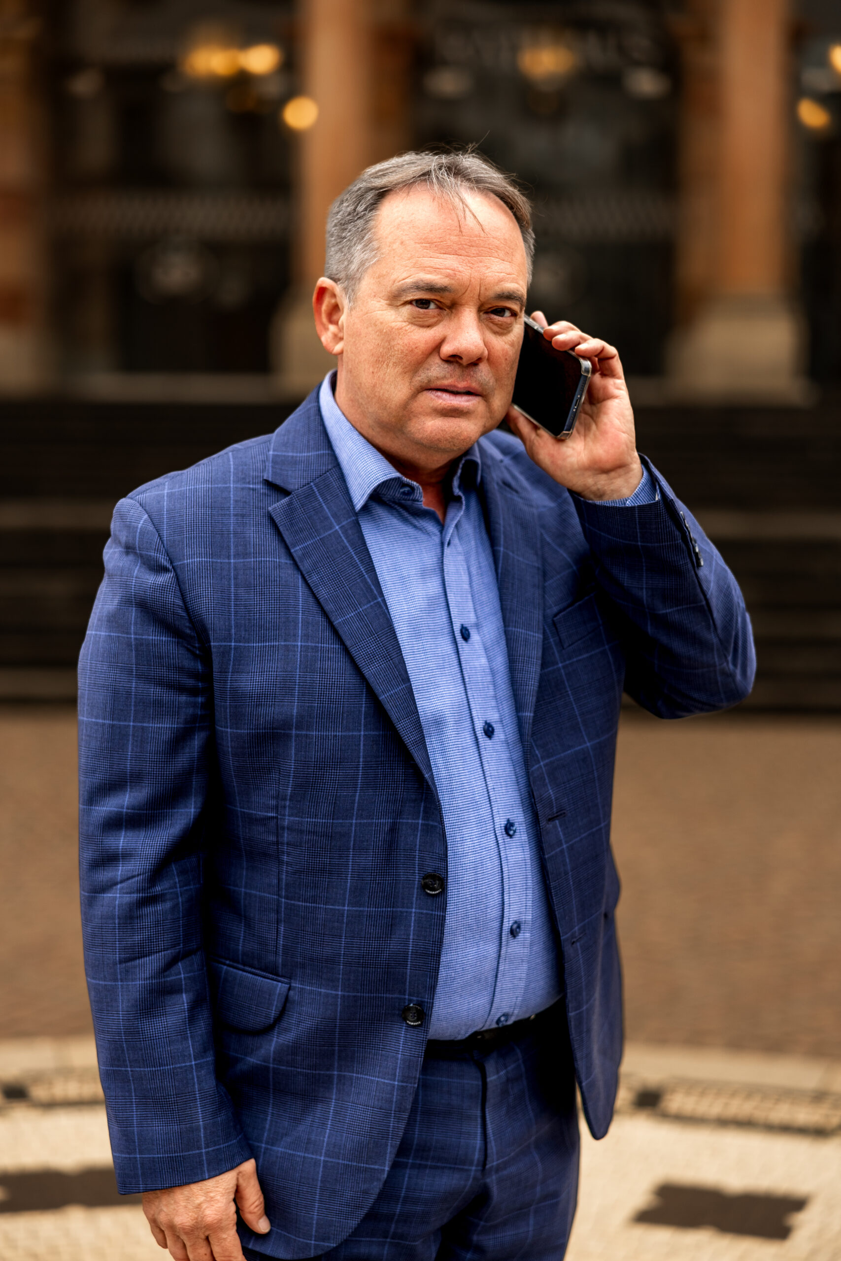 Scott Brokaw taking a phone call wearing a blue suit
