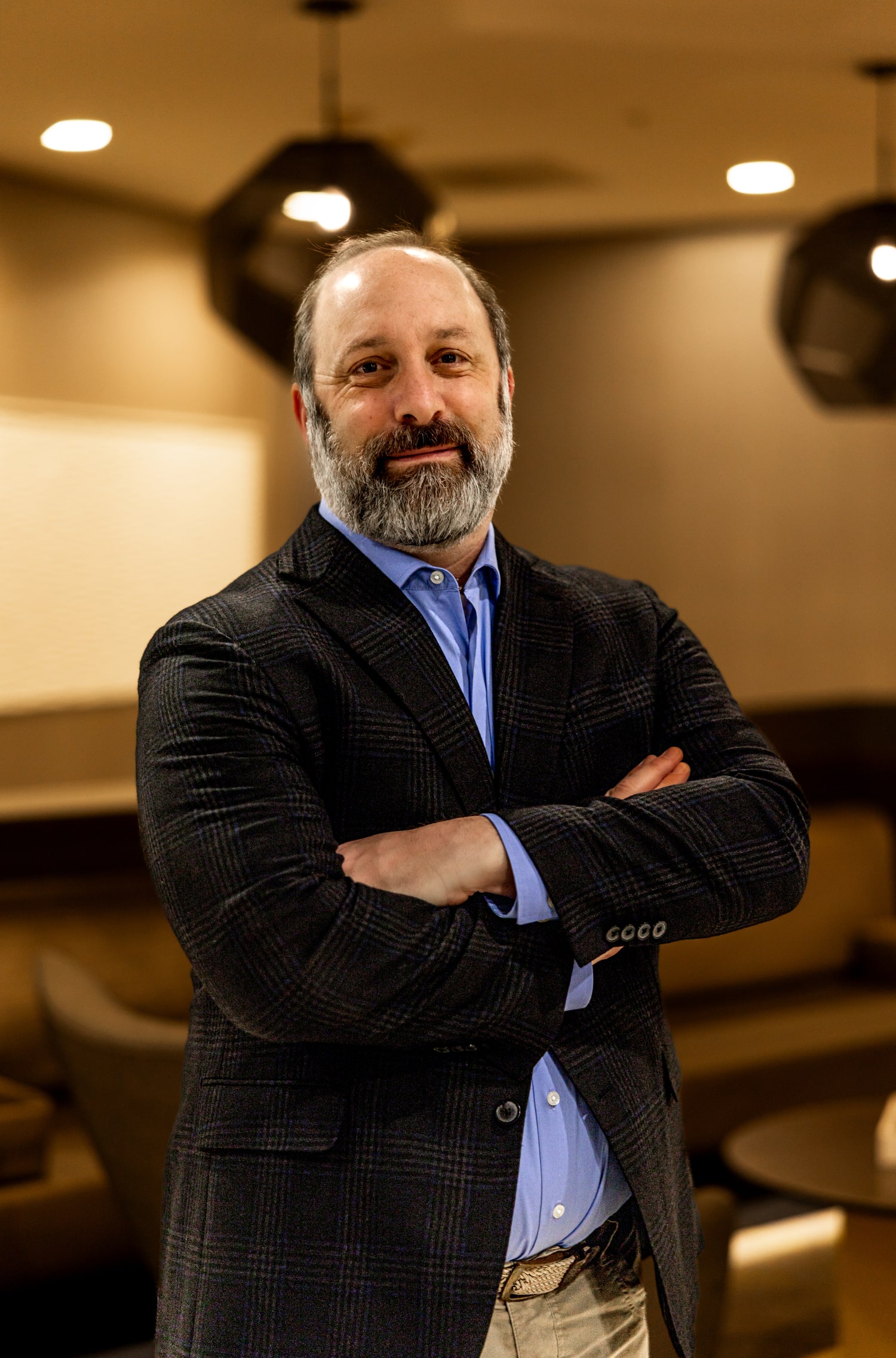 Treb Courie with arms crossed wearing a plaid jacket in a lounge